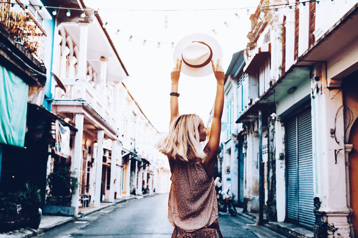 excited woman traveling walking down street holding hat