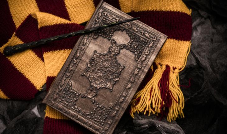 flat lay of red and yellow scarf, wand and wizard book