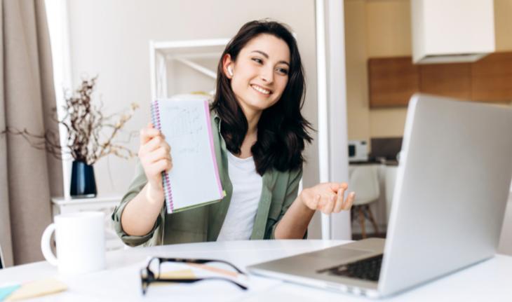 woman holding notebook in front of a laptop